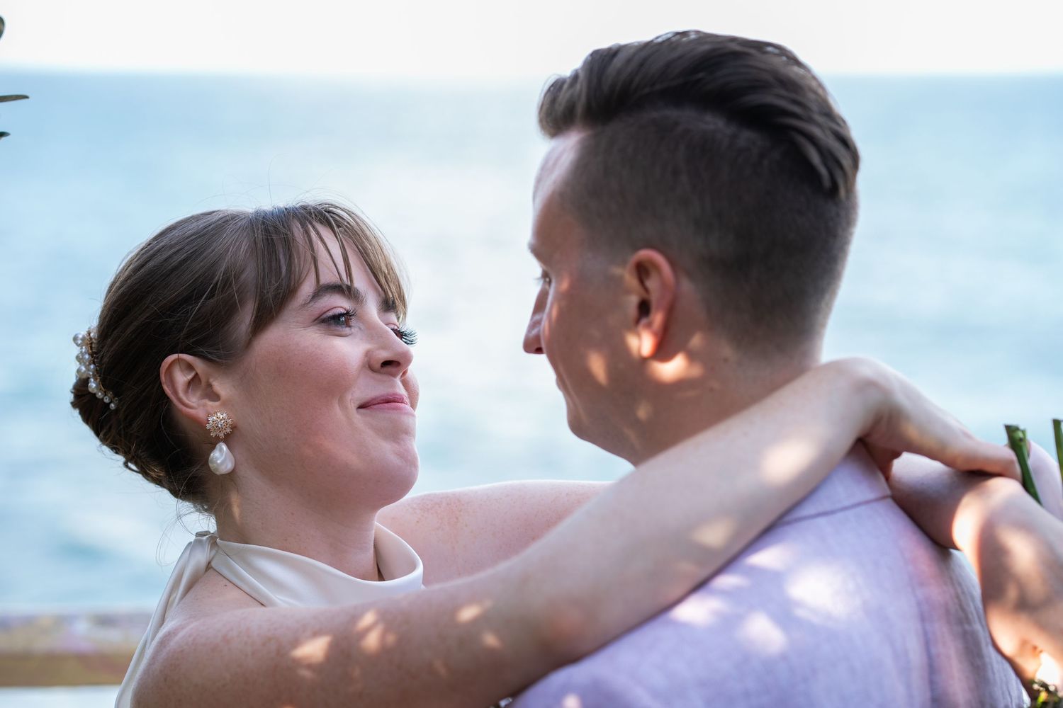 A couple shares an intimate moment against a bright sky backdrop during their wedding photoshoot.