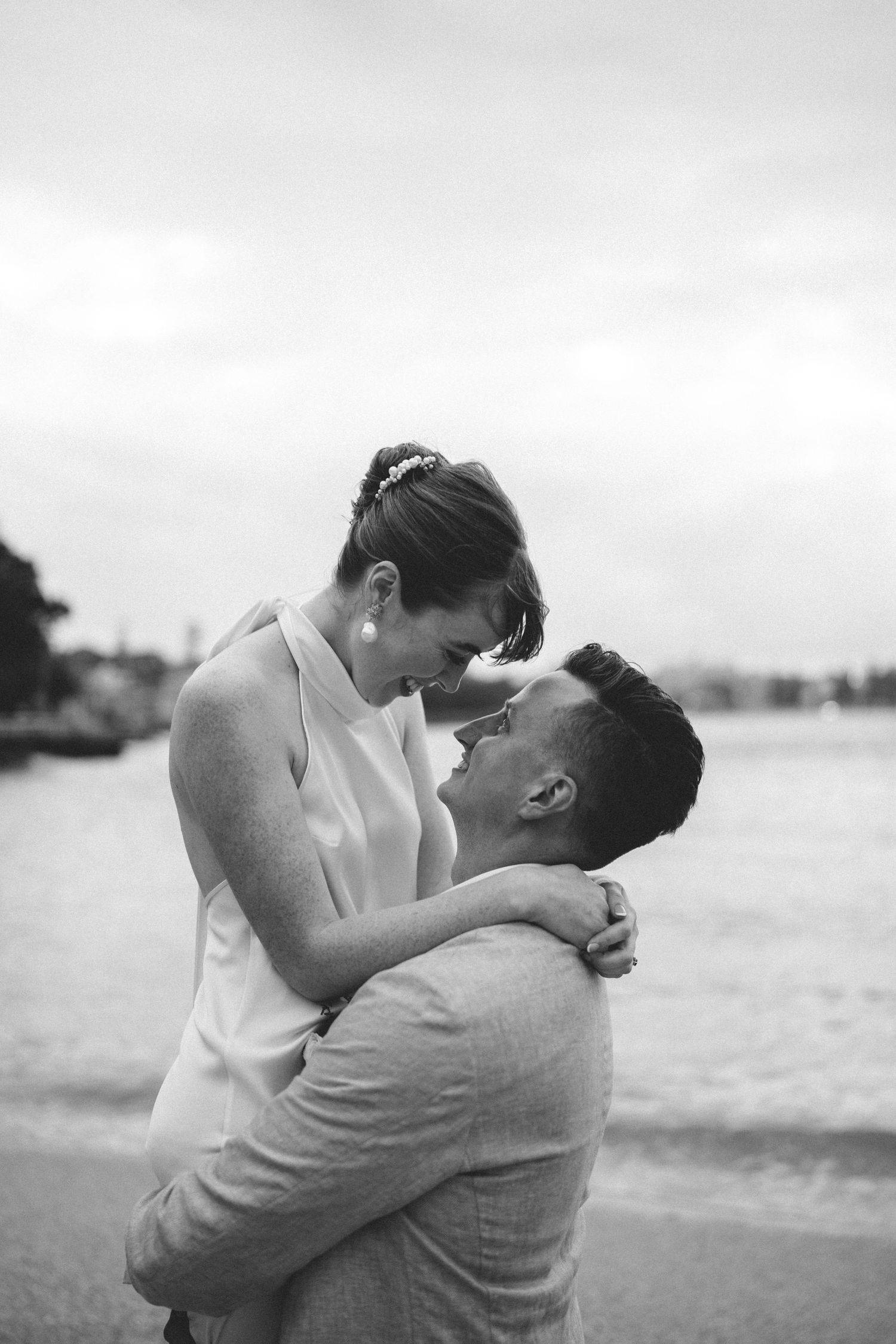 A black and white portrait of a couple sharing an intimate embrace by the water.