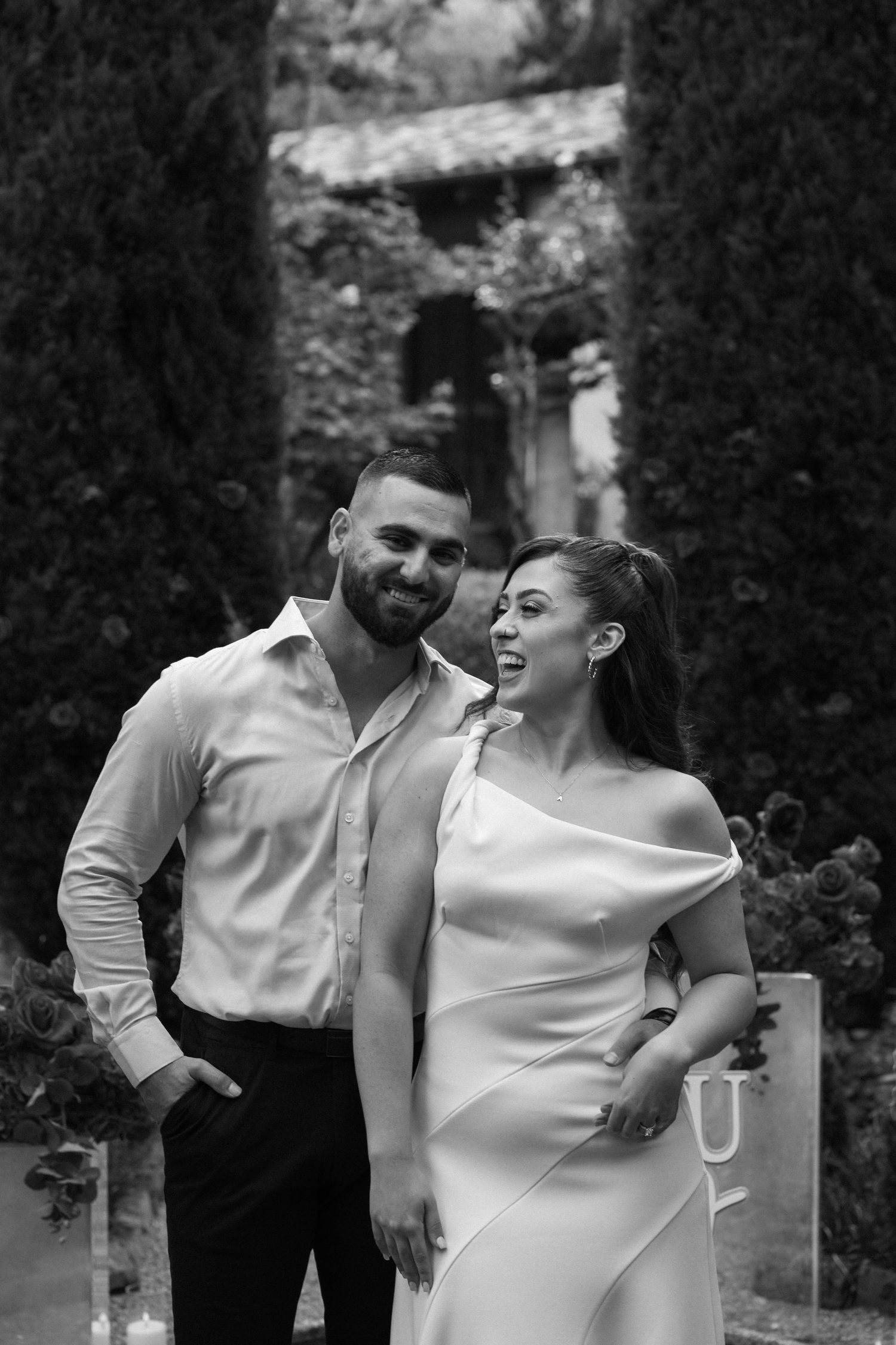 Black and white candid photo of couple laughing together in garden setting.