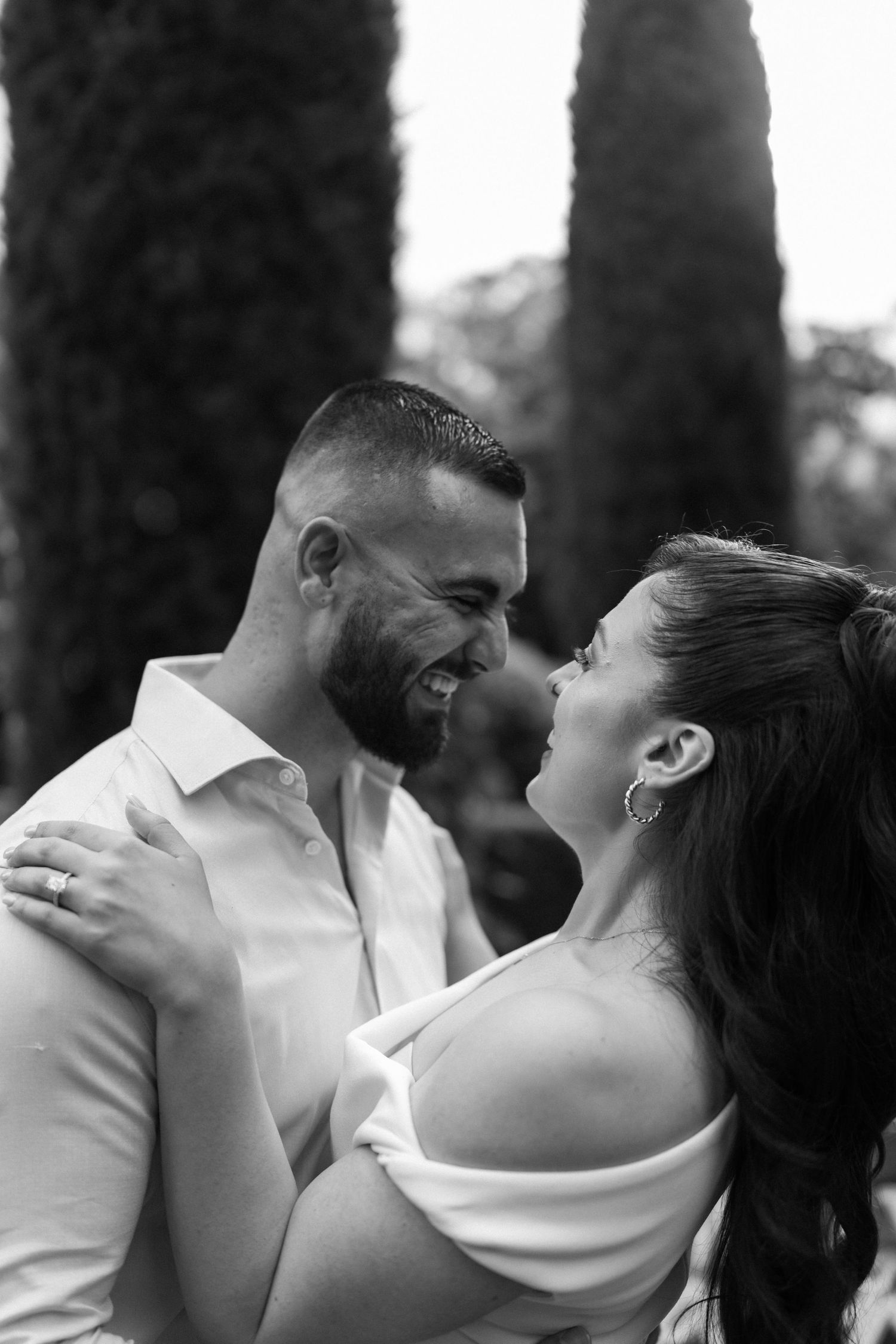Black and white intimate moment between couple among tall cypress trees.