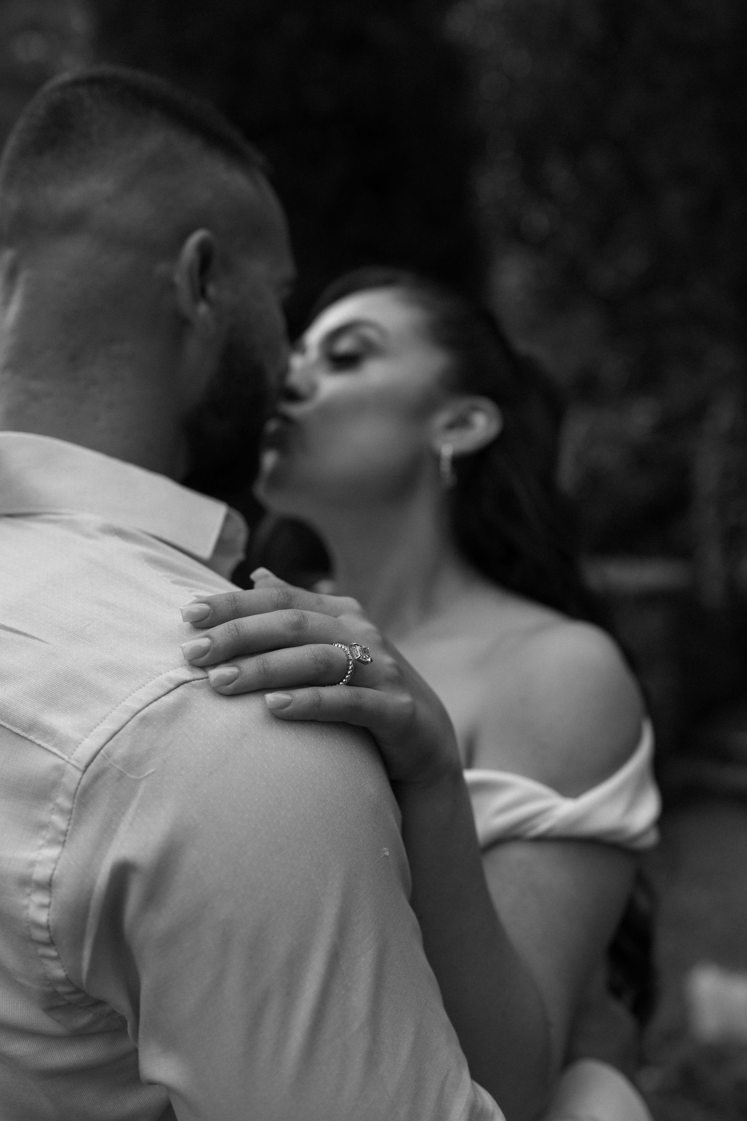 Intimate black and white moment showing engagement ring during romantic embrace.