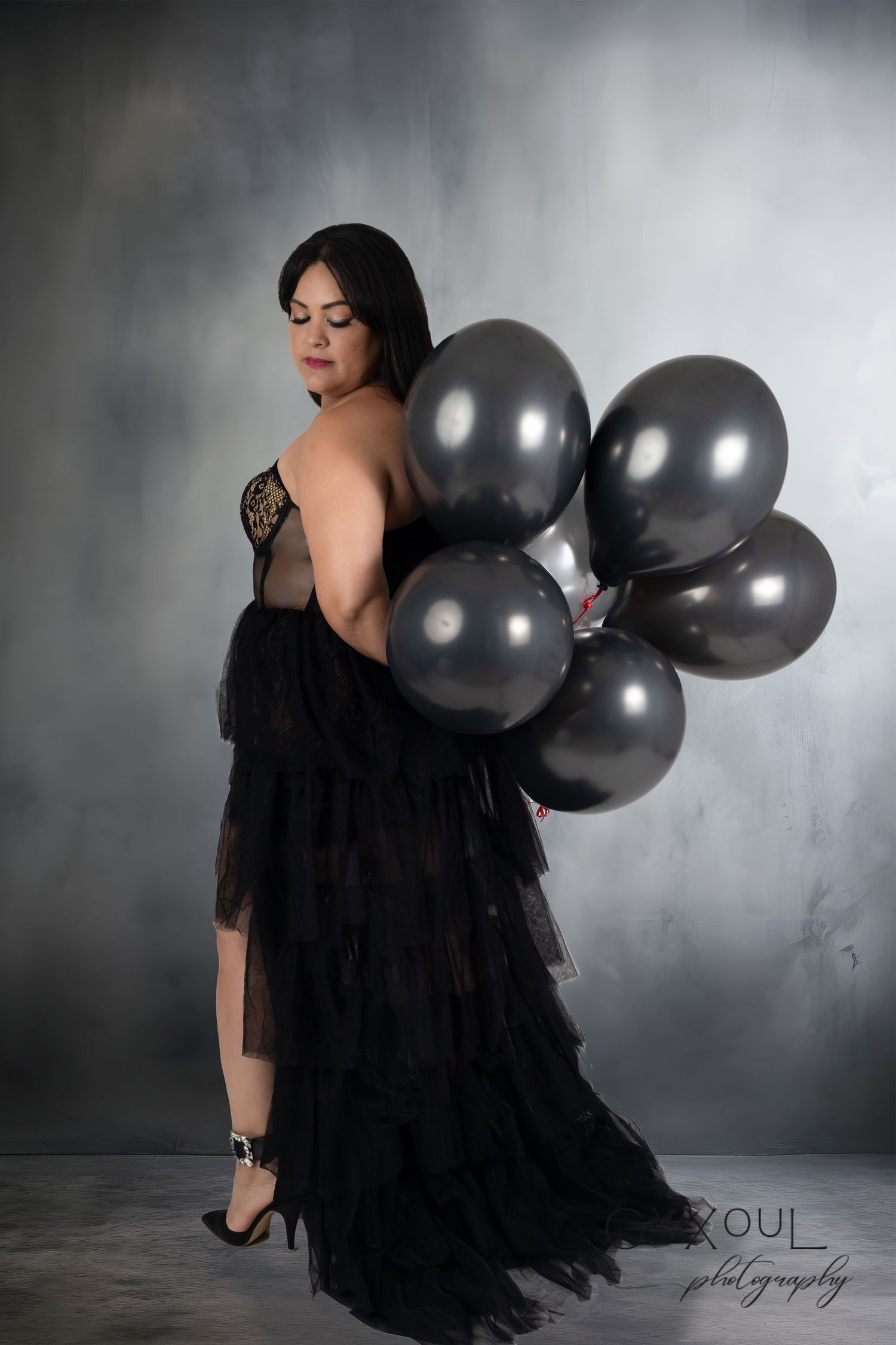 Dramatic portrait with black tulle gown and silver balloons against foggy backdrop.