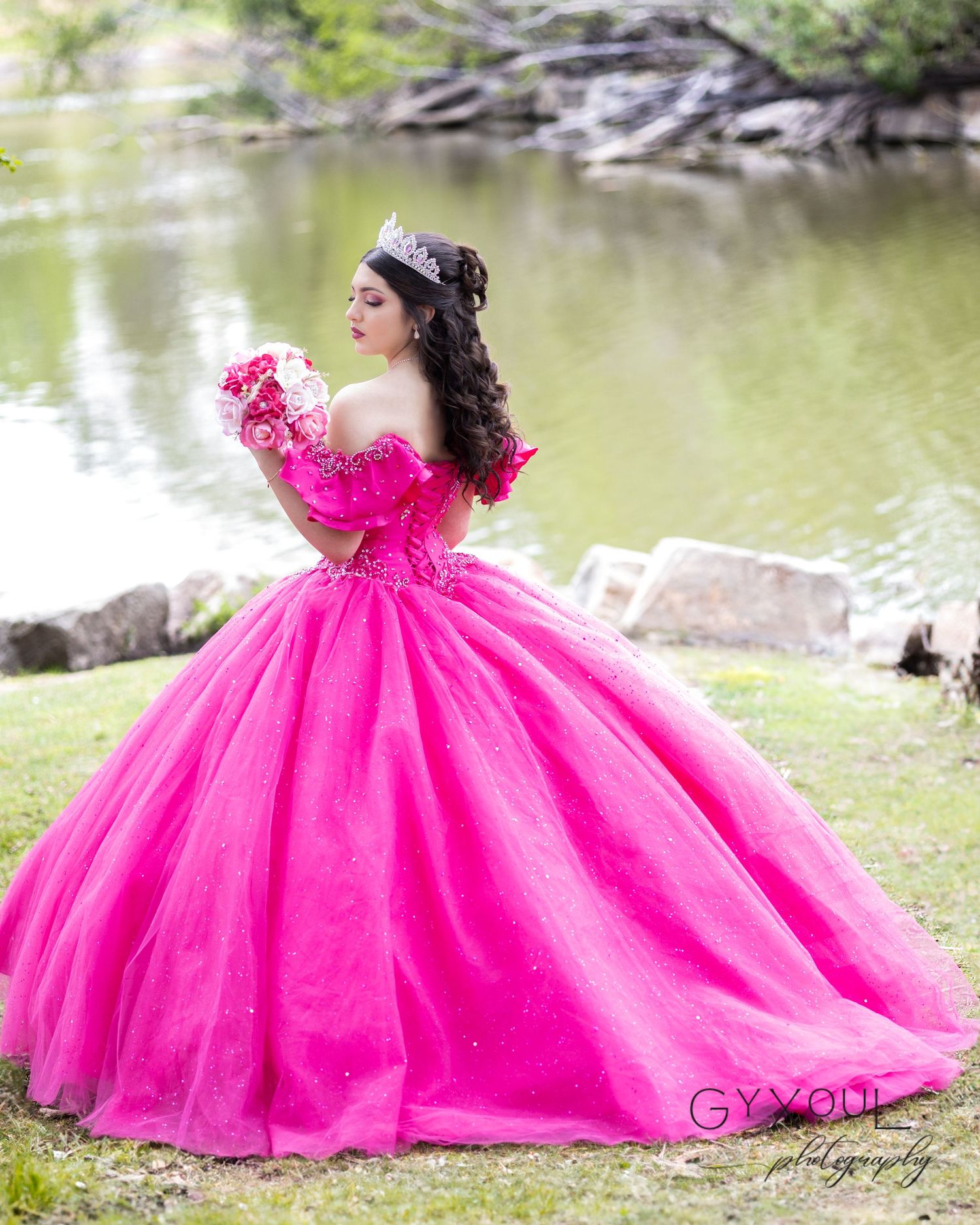 A vibrant hot pink ball gown worn in an outdoor photoshoot near a pond with soft natural lighting.