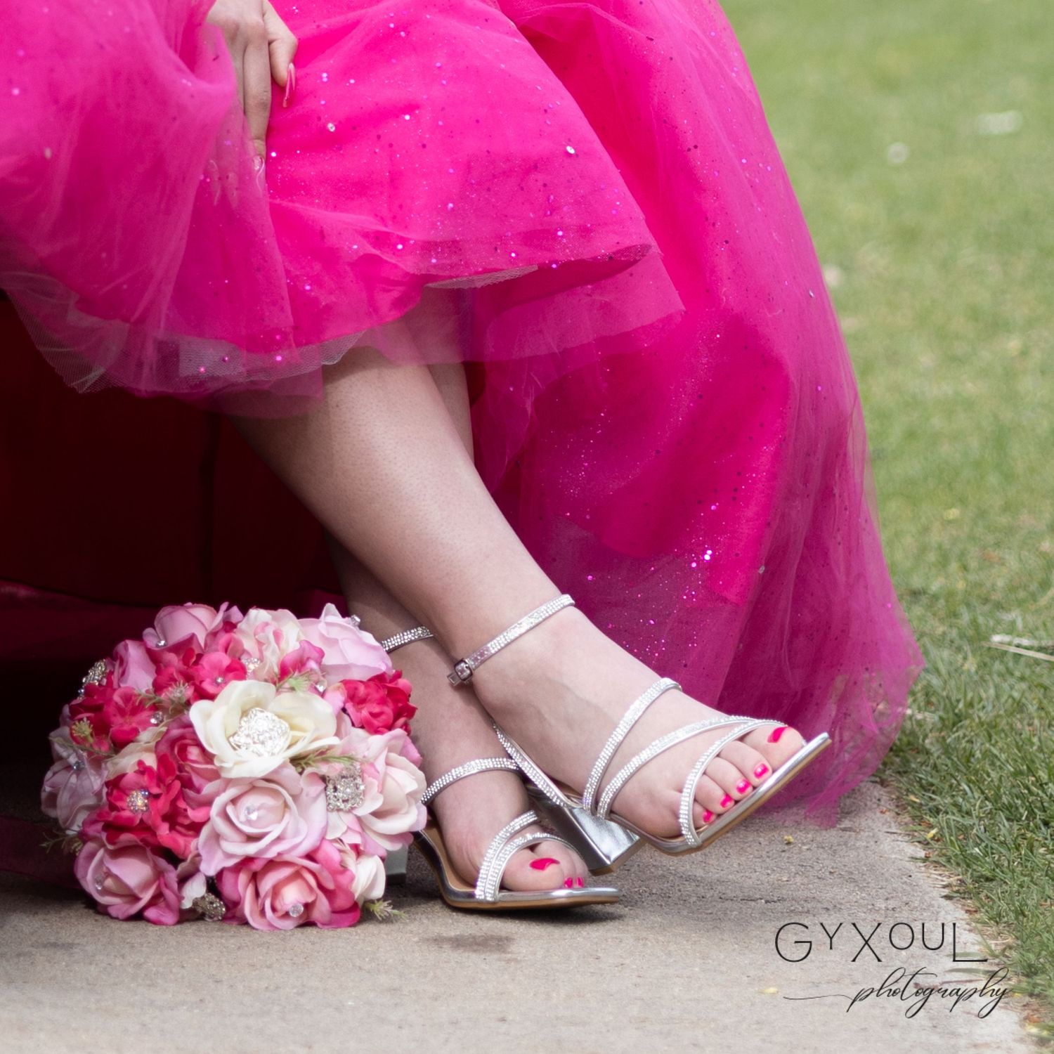Close-up of silver sandals and pink rose bouquet next to flowing pink tulle dress.