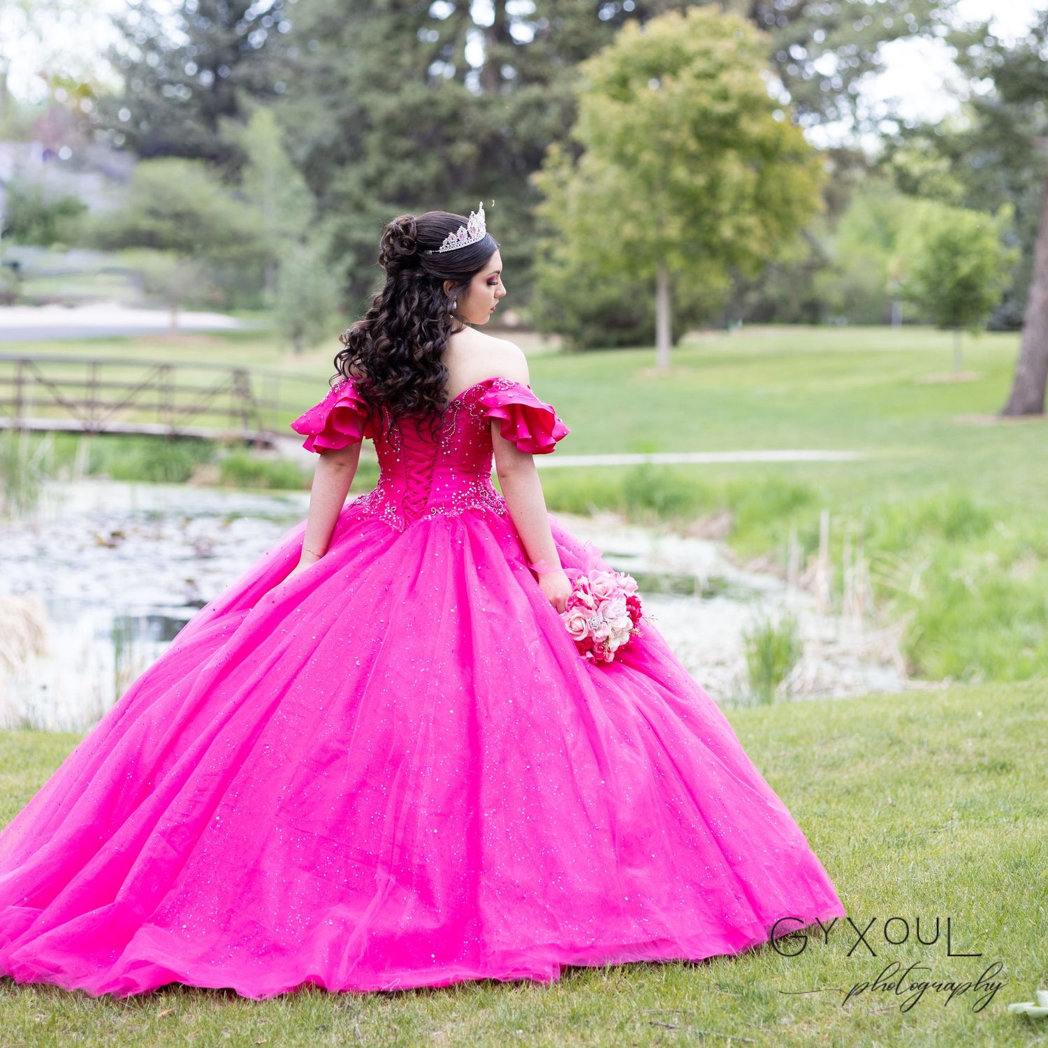 Back view of a dramatic hot pink ball gown with off-shoulder details in an outdoor setting.
