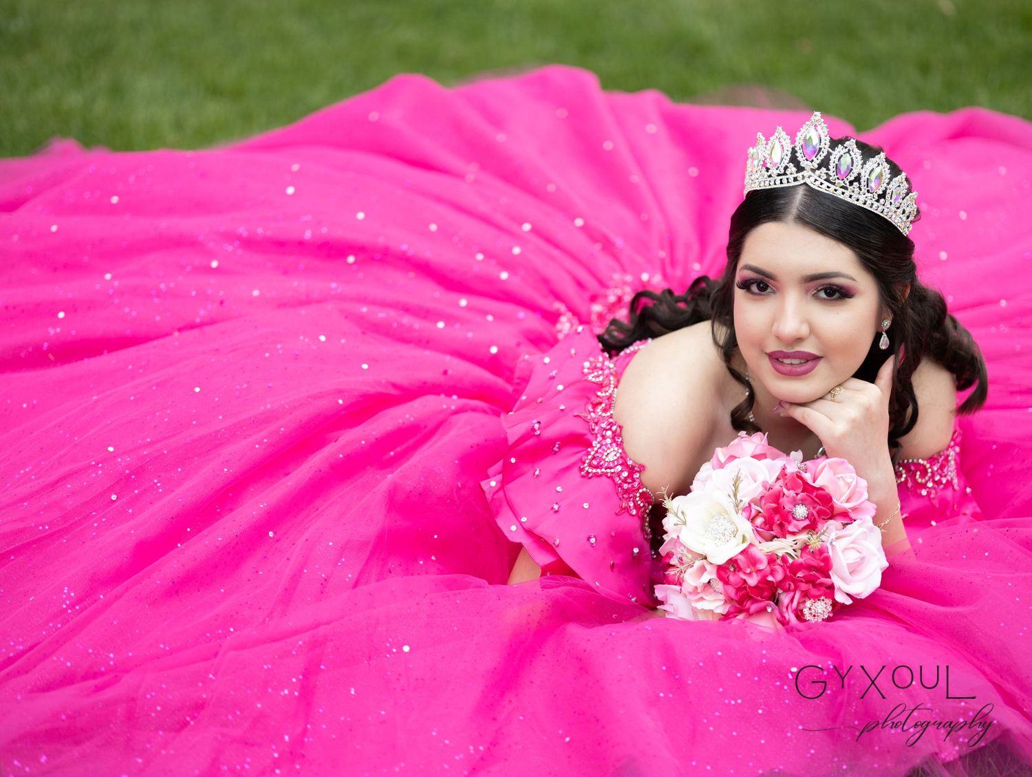 Dramatic hot pink ball gown spread out on grass with crystal tiara and floral accents.
