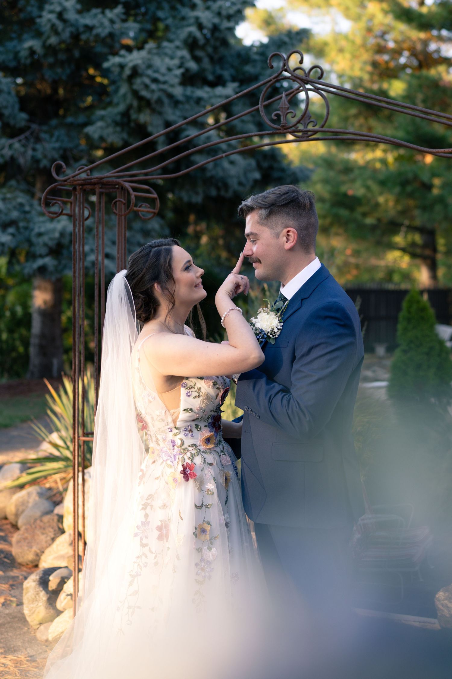 Romantic moment between newlyweds under a decorative garden arch during their outdoor wedding.