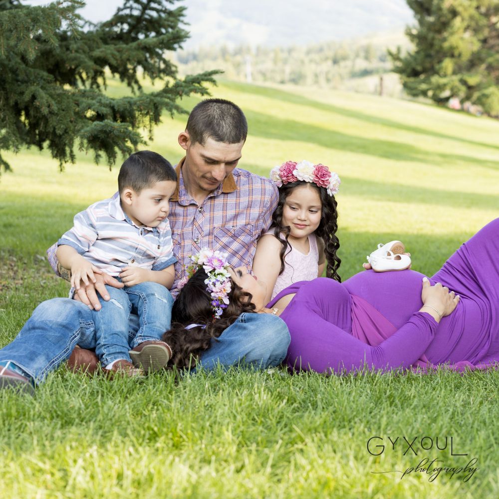 A family relaxes together on green grass with their small dog during an outdoor photo session.