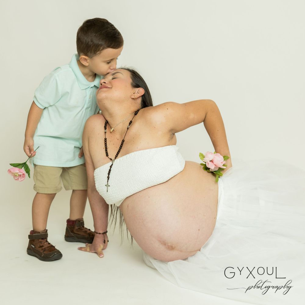 A tender maternity moment captured in studio with gentle lighting and neutral tones.