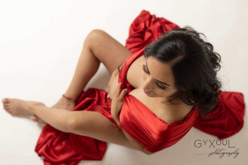 Professional maternity photo featuring elegant red satin fabric draping in artistic boudoir pose.