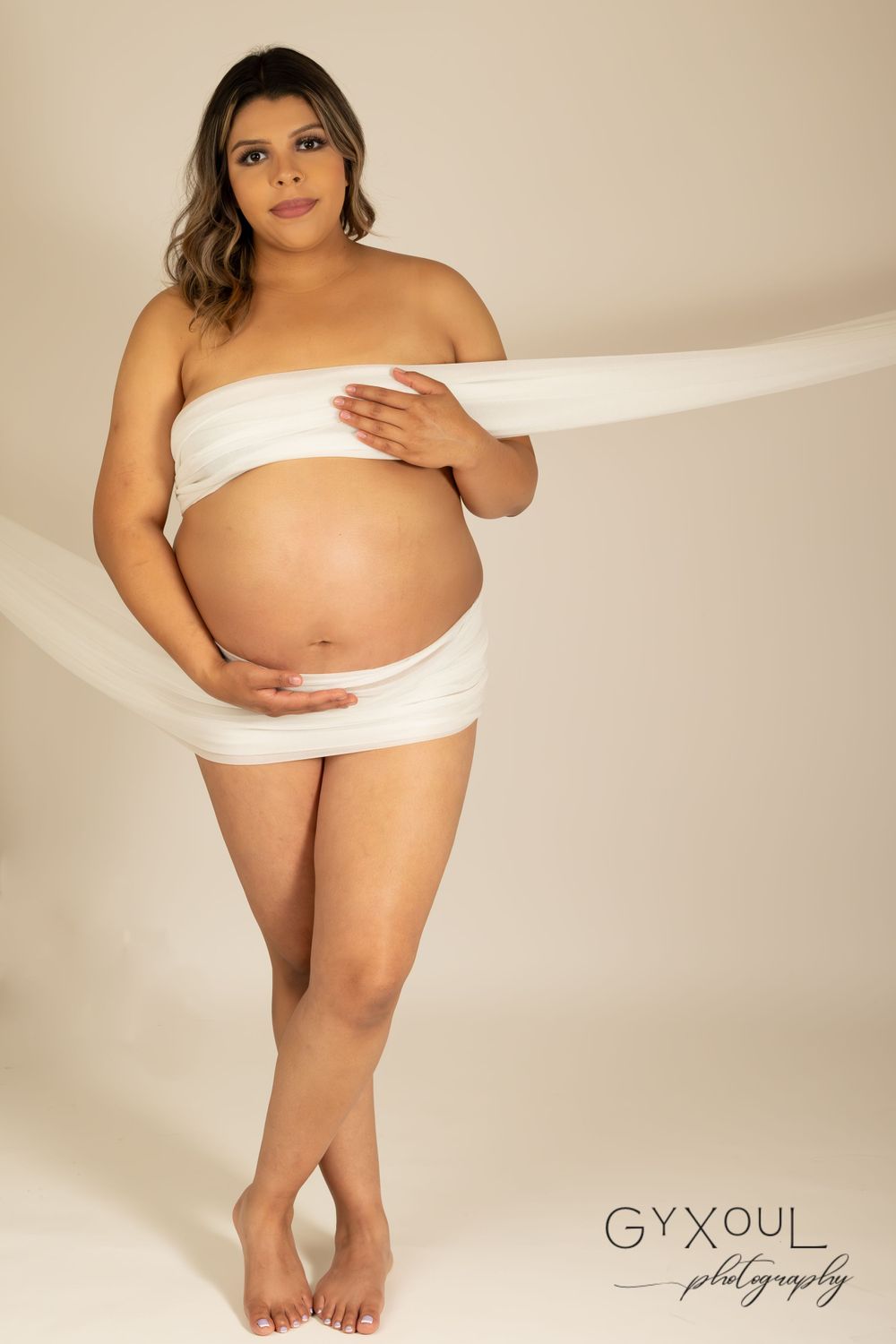 Artistic maternity portrait with white fabric wrap against neutral backdrop.