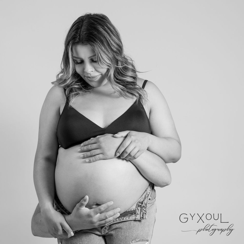 Black and white maternity portrait showing a tender moment with hands on belly.