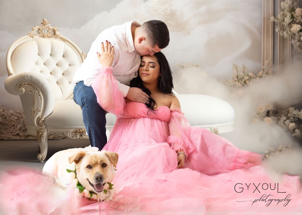 Romantic maternity scene on vintage chaise with couple and golden retriever in pink setting.