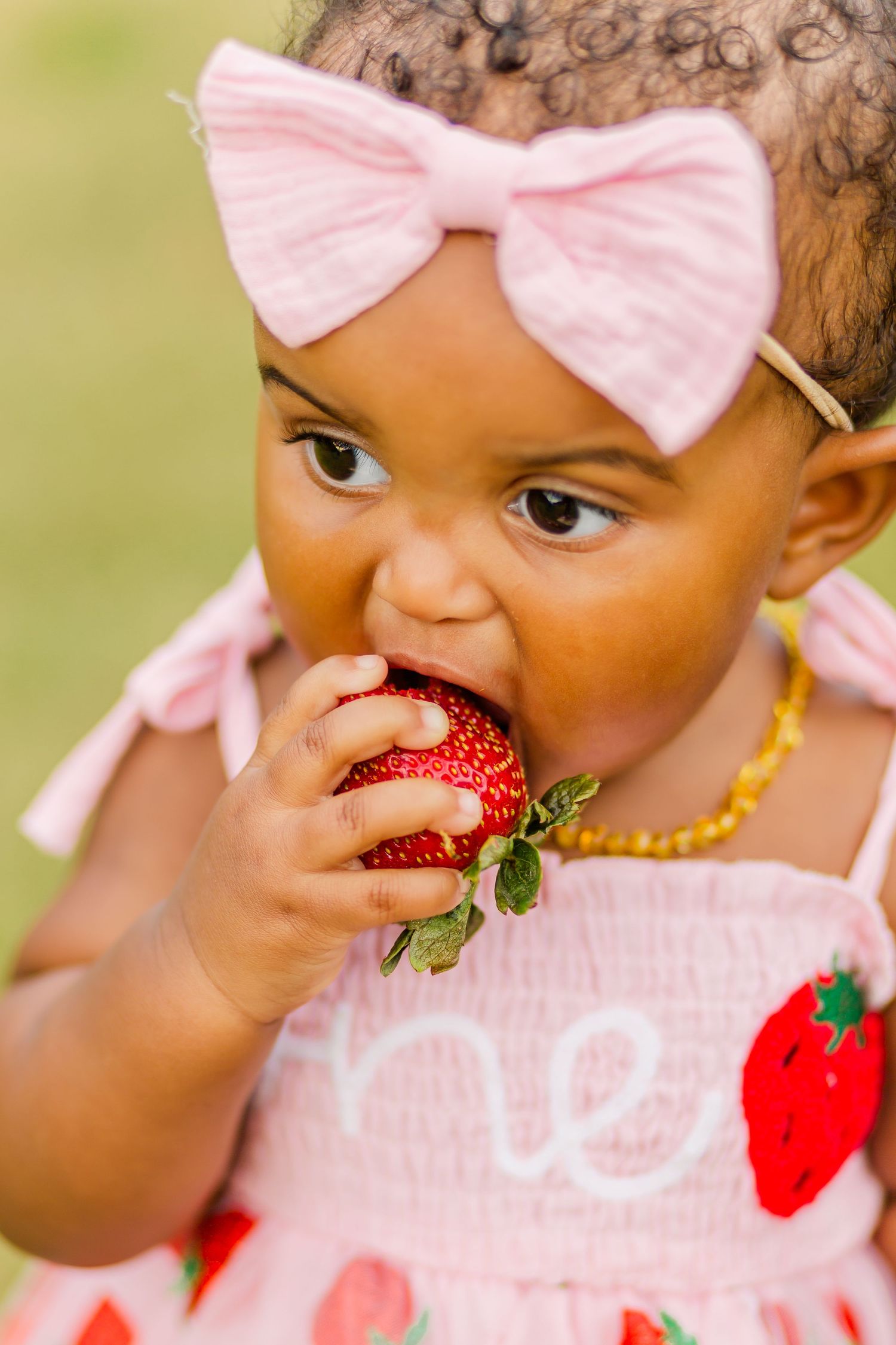 A baby in pink takes a big bite of a fresh red strawberry during a photo shoot.