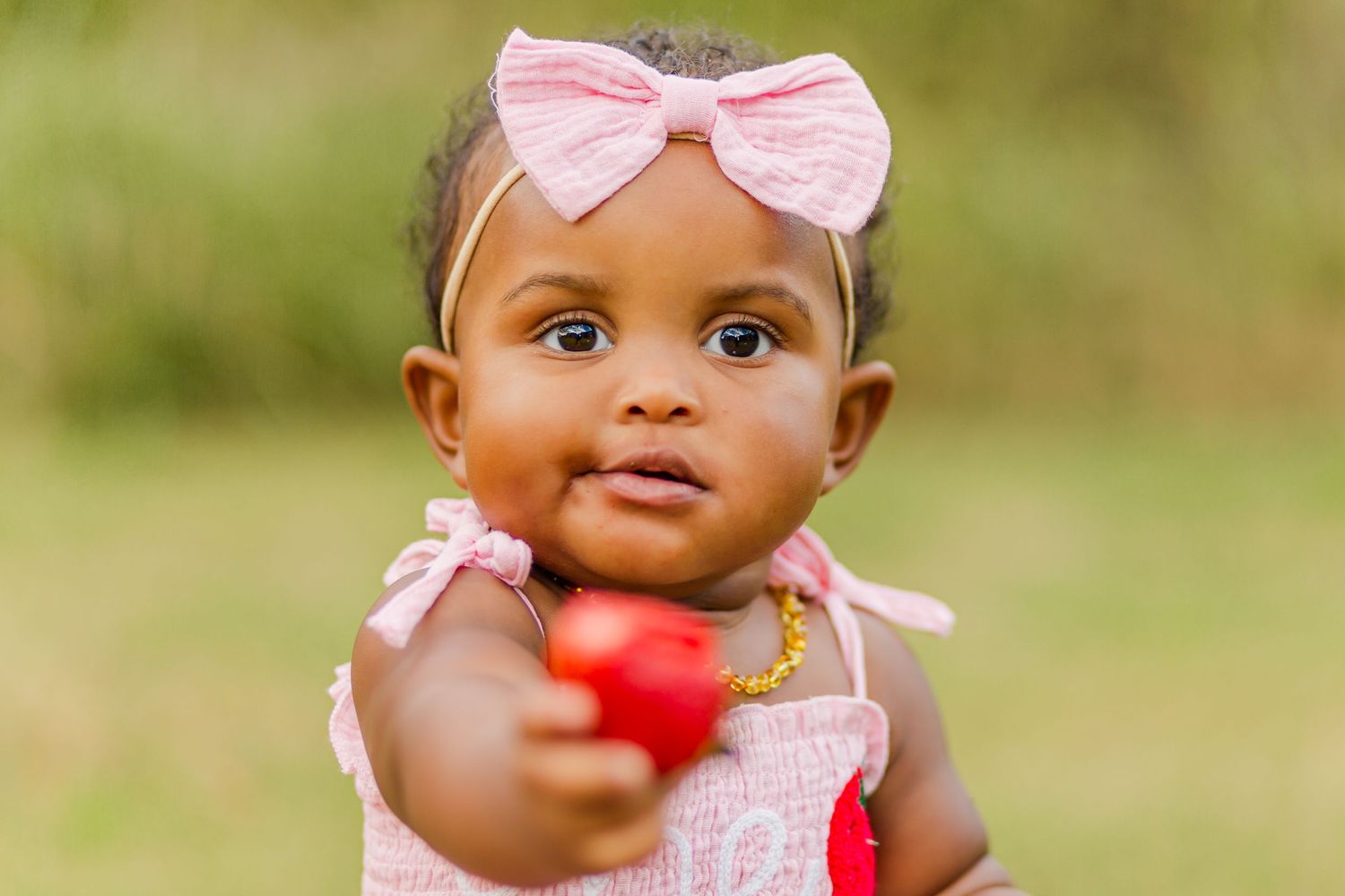 A baby in pink reaches towards the camera during an outdoor photo session.