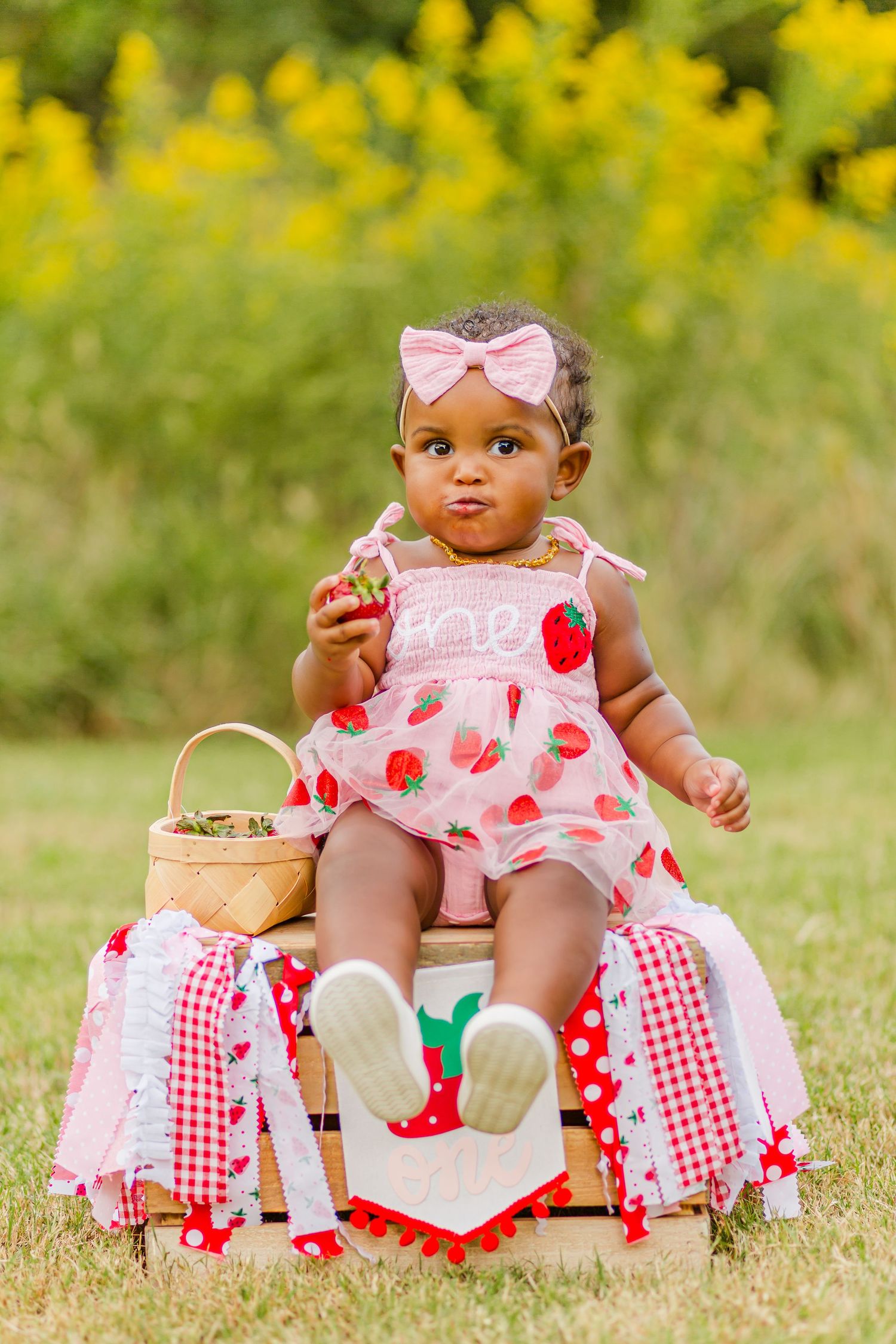 A pink strawberry-print dress and matching bow on a sunny outdoor setting with red and white checked decorations.