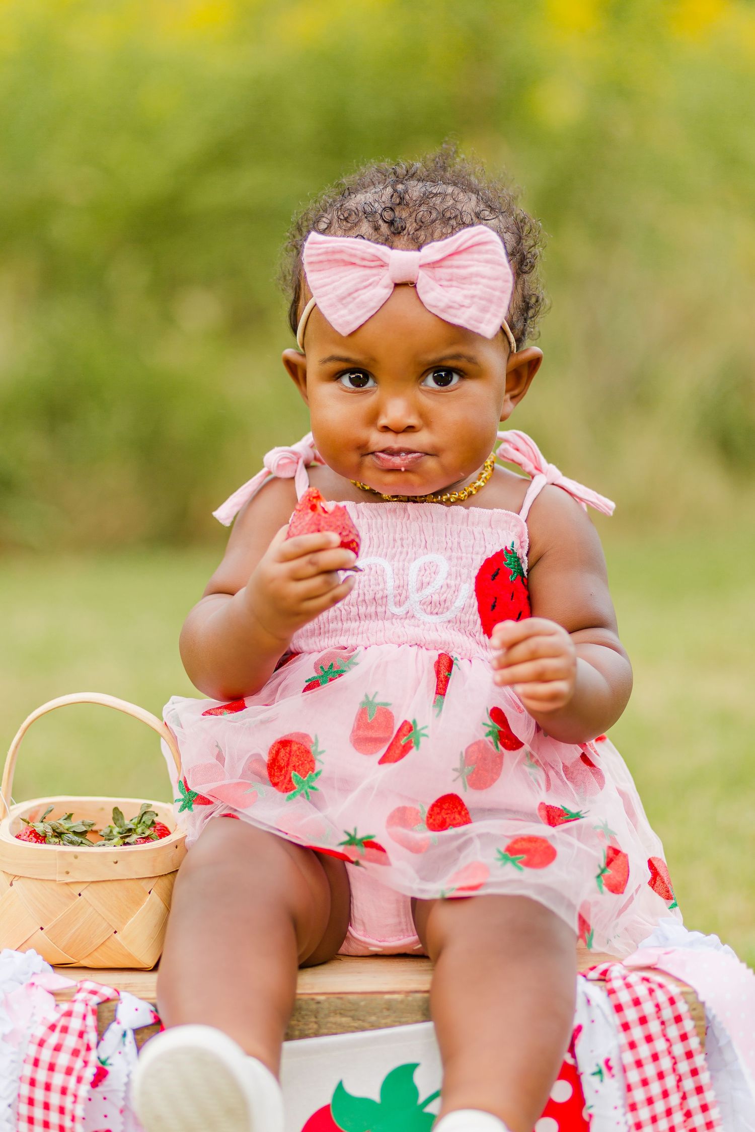 Close-up view of a pink strawberry dress and bow against a sunny yellow background.