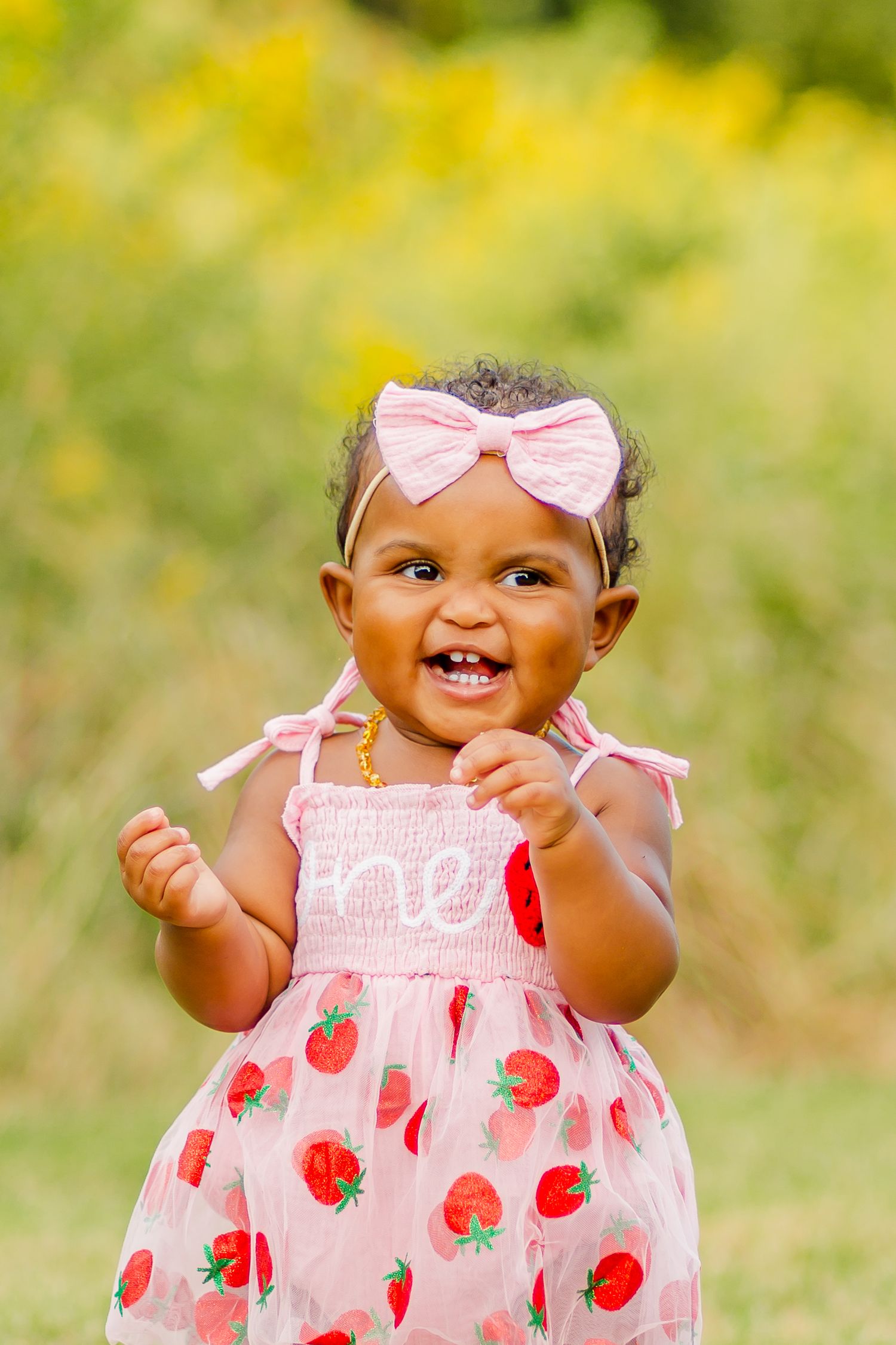 Adorable baby wearing pink strawberry dress and bow smiling brightly.