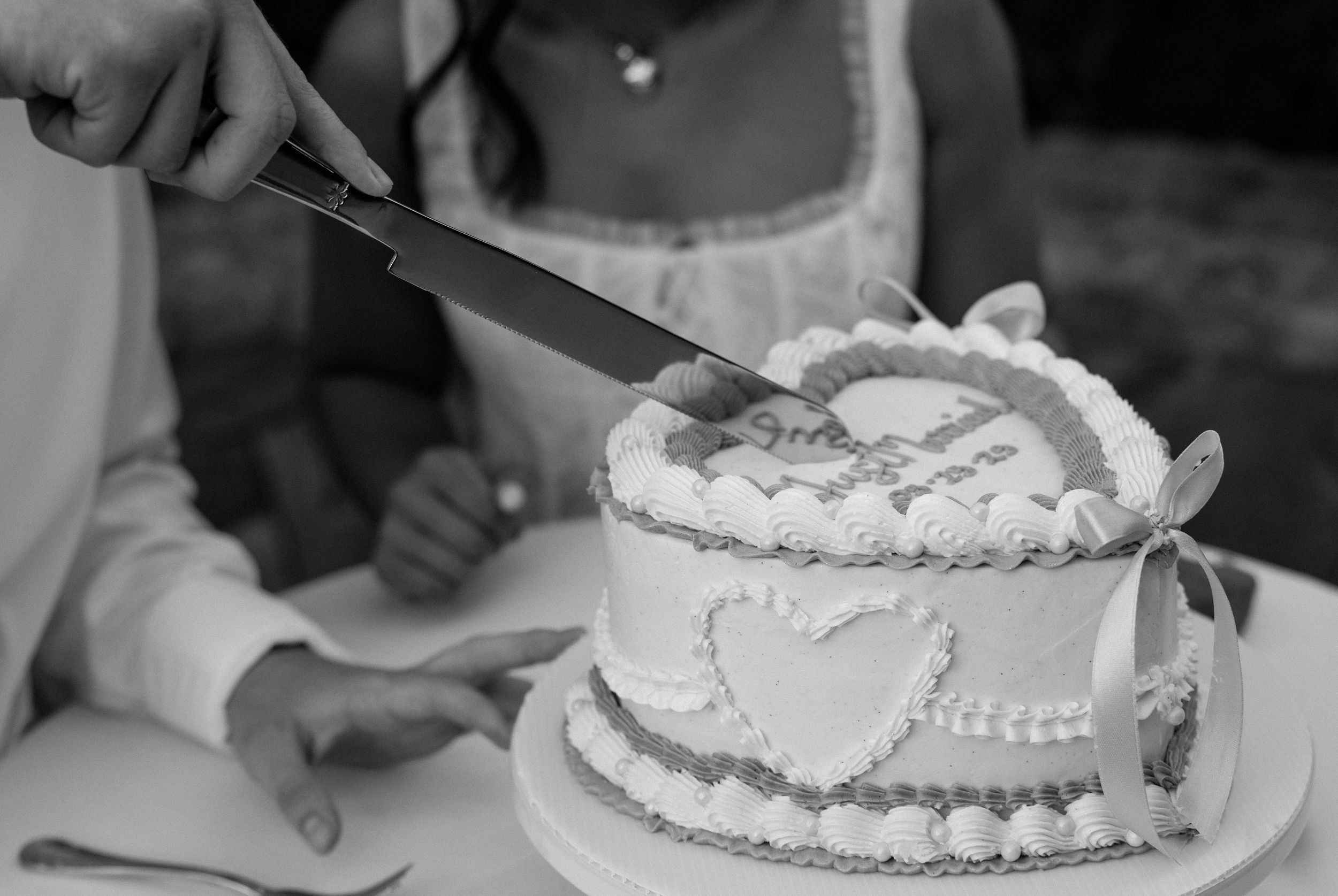 Black and white photo sequence showing hands cutting and serving slices of a decorated wedding cake at a reception.
