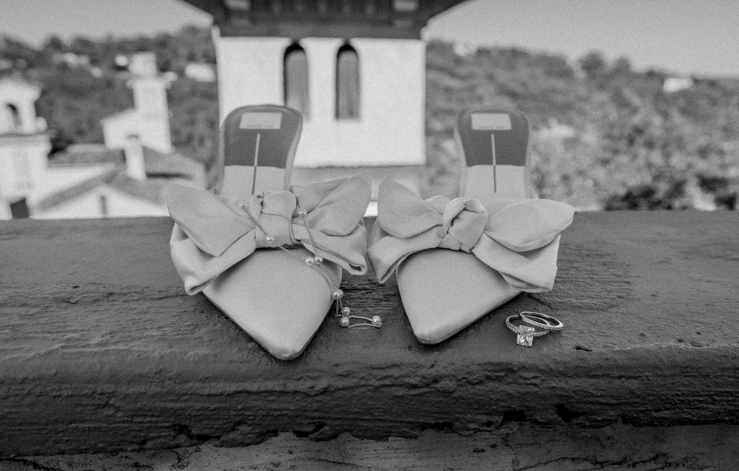A pair of white leather bow shoes sits on a dark surface with a church steeple visible in the background.
