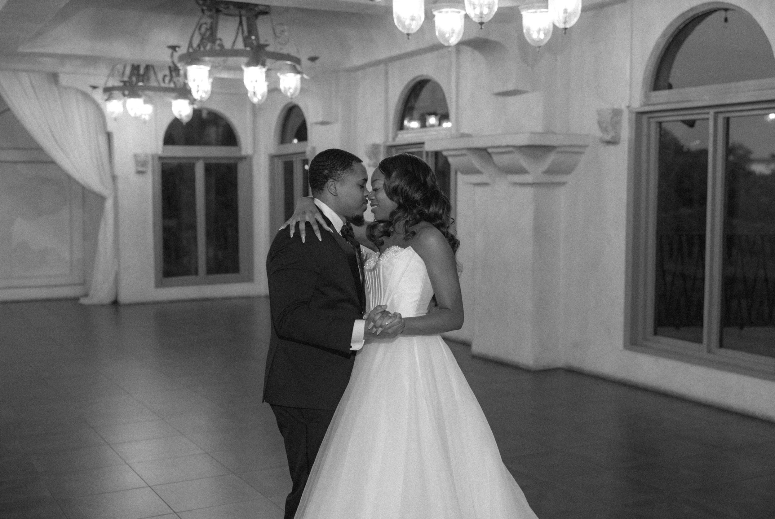 A romantic black and white photo of a newly married couple sharing their first dance in an elegant ballroom.