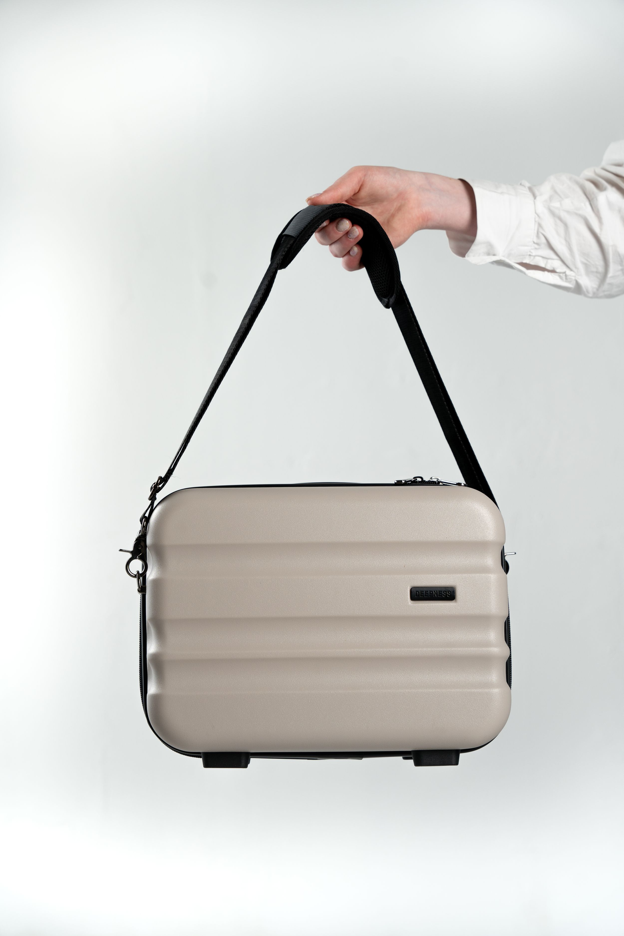 Hand holding a beige hardshell carrying case with black shoulder strap against white background.
