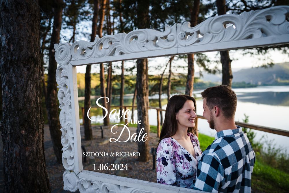 A save the date photo in an ornate white frame featuring a couple by a lake at sunset.