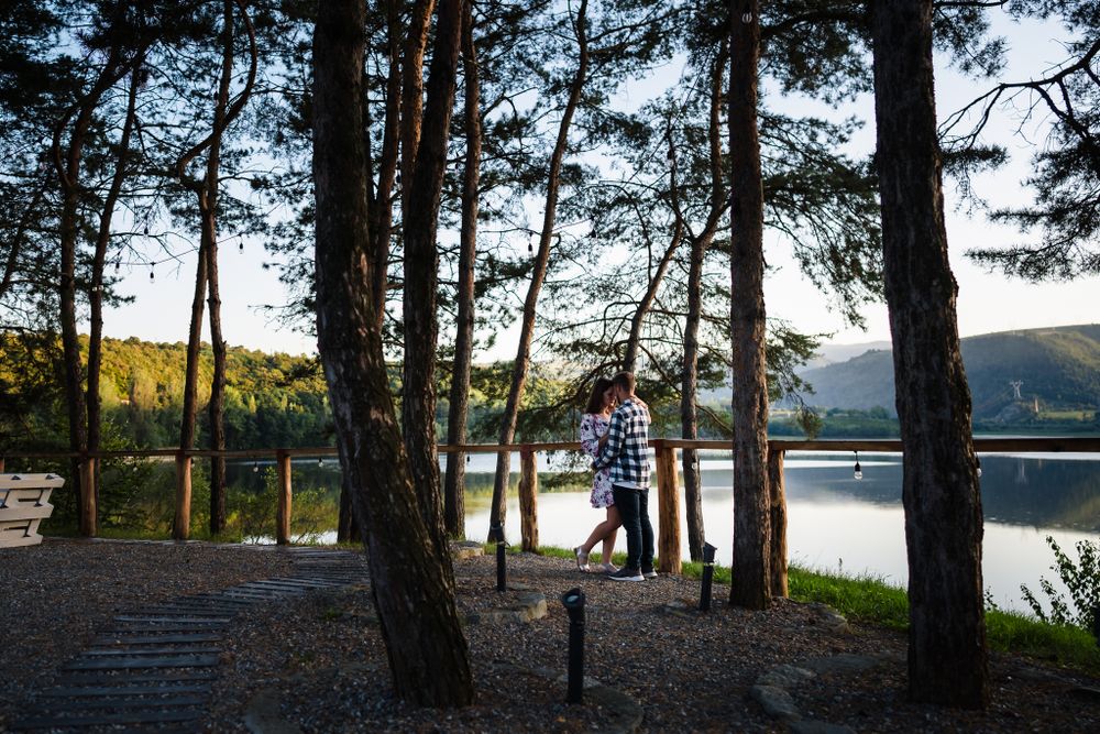 Scenic lakeside engagement photo session at sunset with tall pine trees framing the water view.