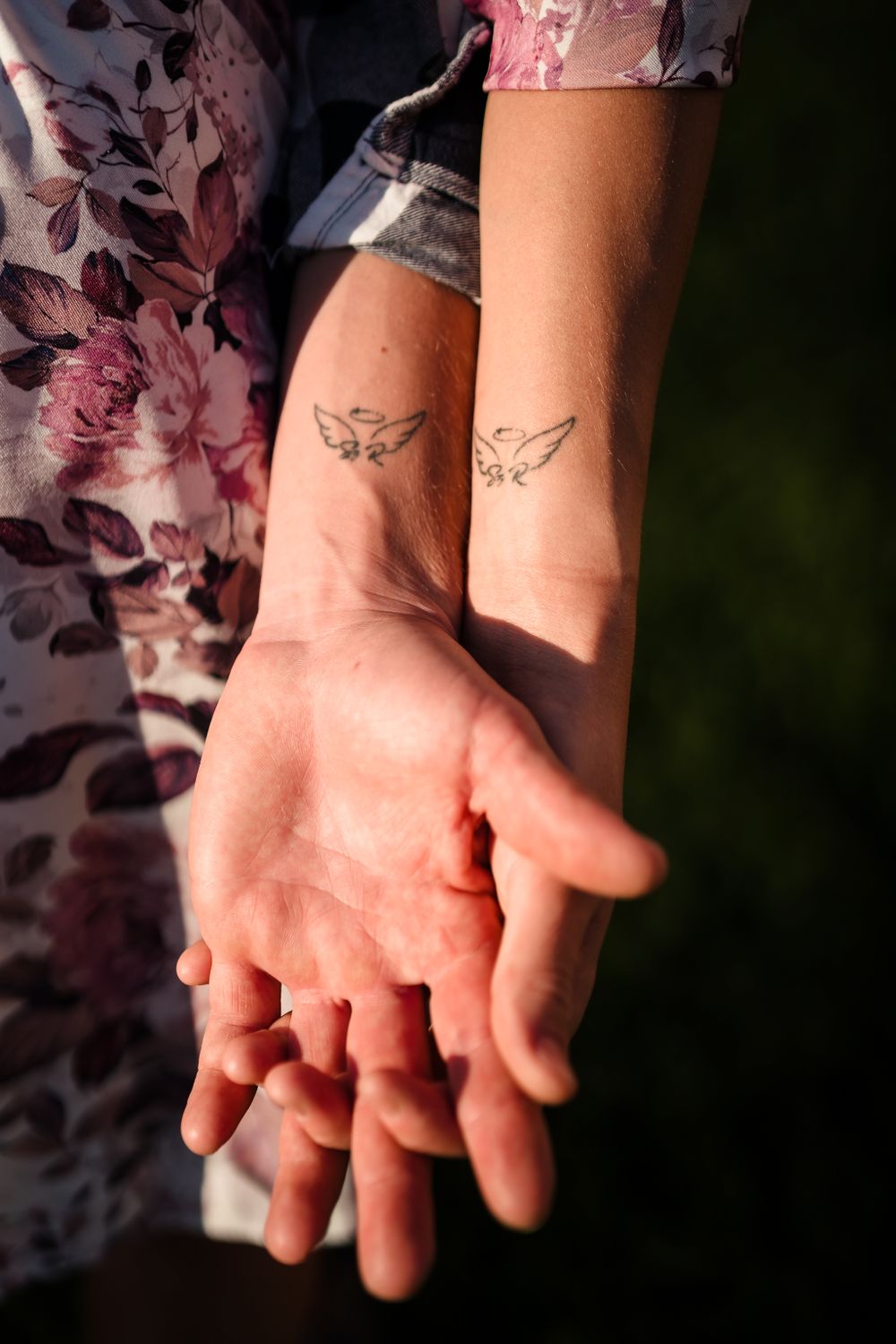Close-up of matching bird tattoos on forearms against a floral dress pattern.