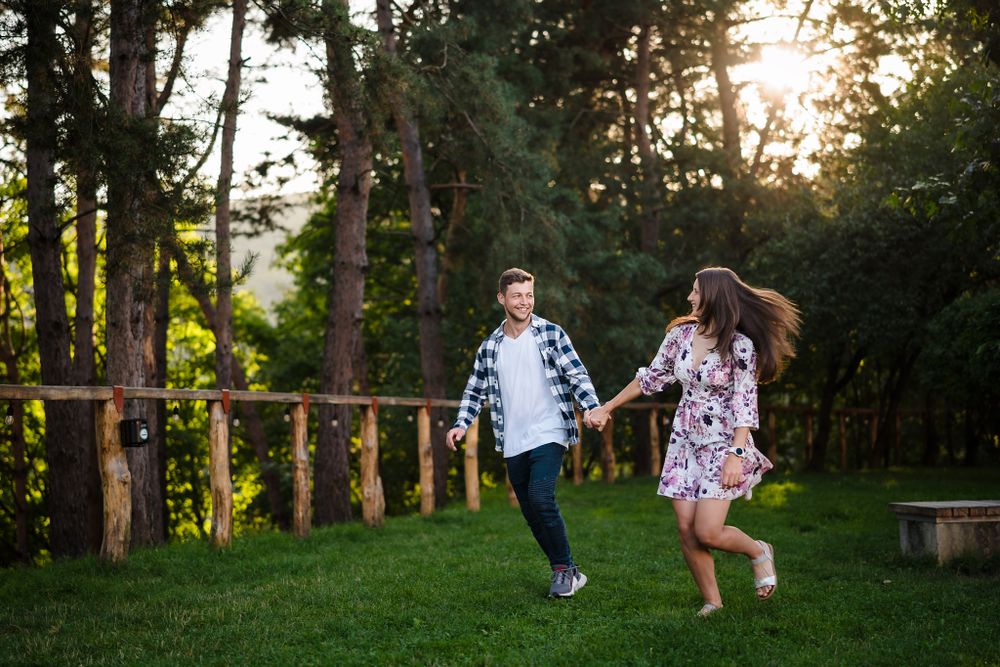 Couple walking together through a wooded park path during golden hour.
