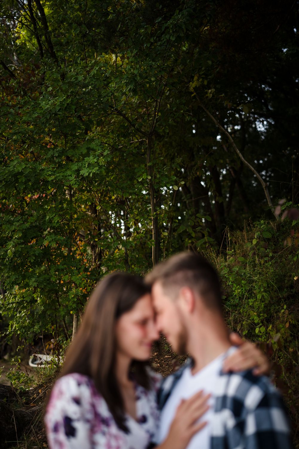 Couple embracing in a lush green forest setting during golden hour.