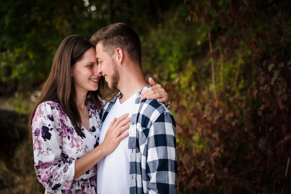 A romantic couple shares an intimate moment outdoors wearing floral and plaid patterns against a natural backdrop.
