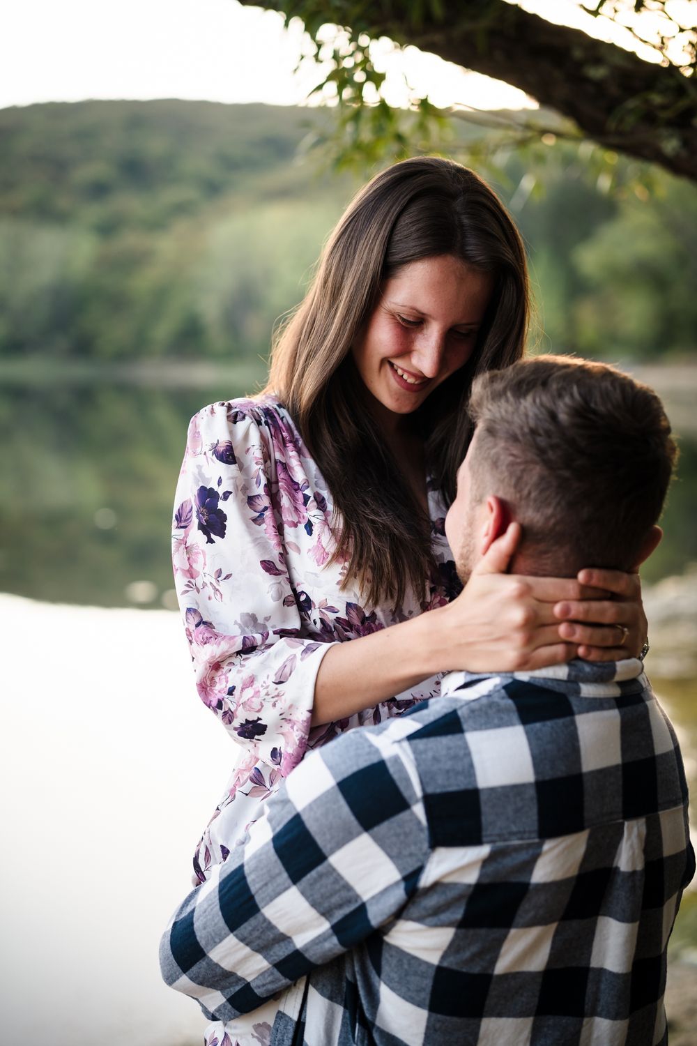 A tender moment captured between a couple by a serene lake with mountains in the background.