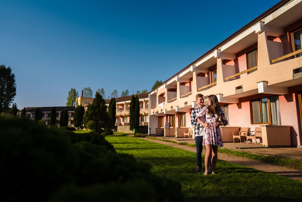 A couple stands in front of a peach-colored apartment building on a sunny day.