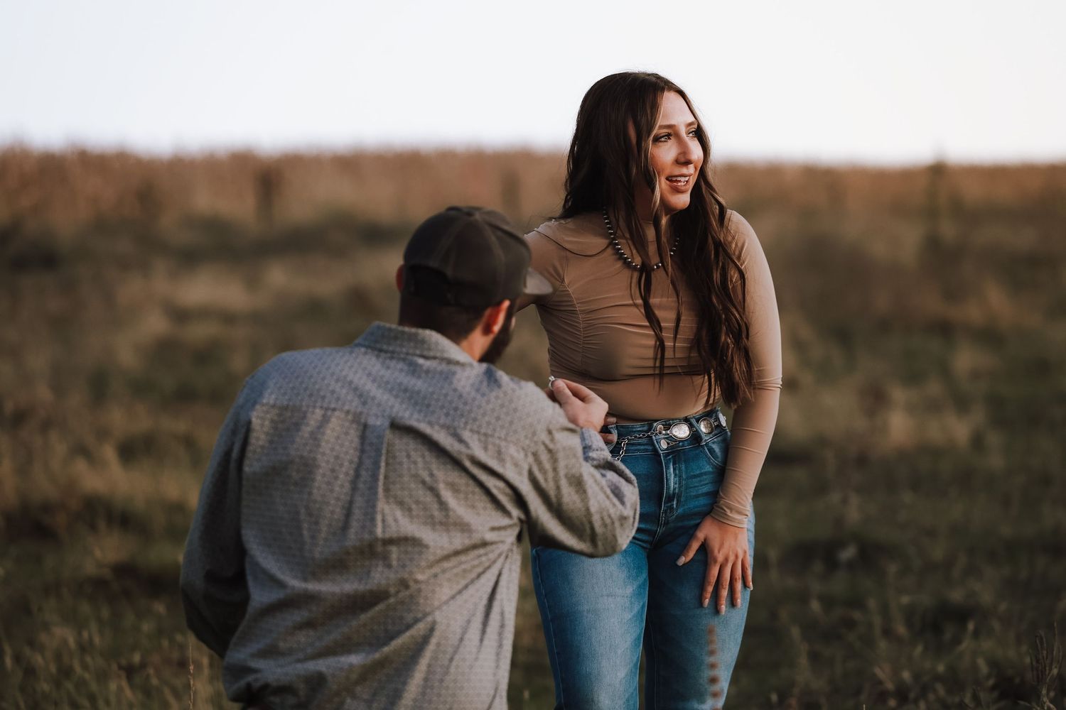 A candid proposal moment captured in a golden field at sunset.