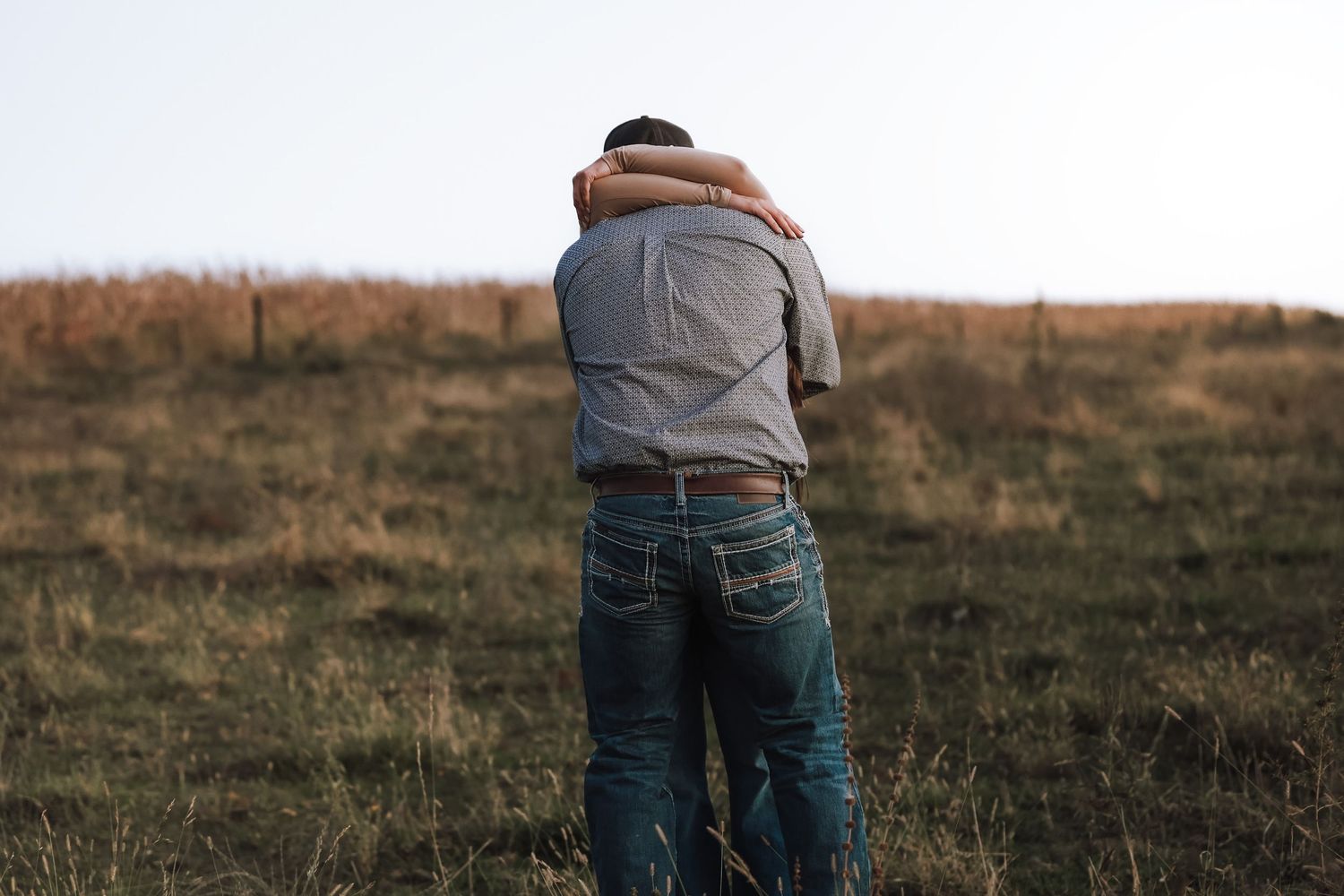 A person kneeling in front of their partner in an outdoor field during a proposal.