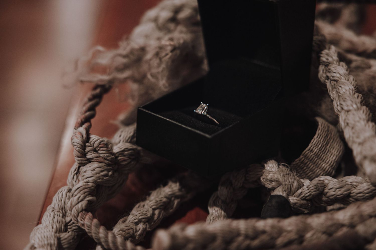 An engagement ring in a black box nestled among rustic rope details.