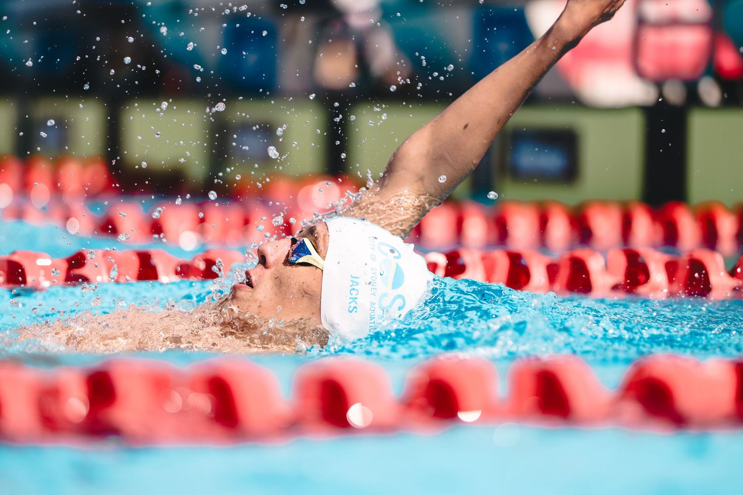 Competitive swimmer performing backstroke in a pool with red lane dividers.
