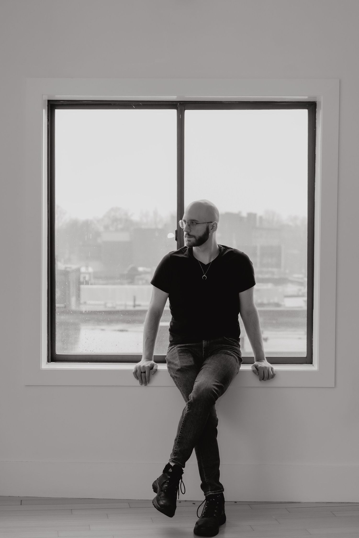 A front facing portrait of Michael in black and white leaning against the window sill