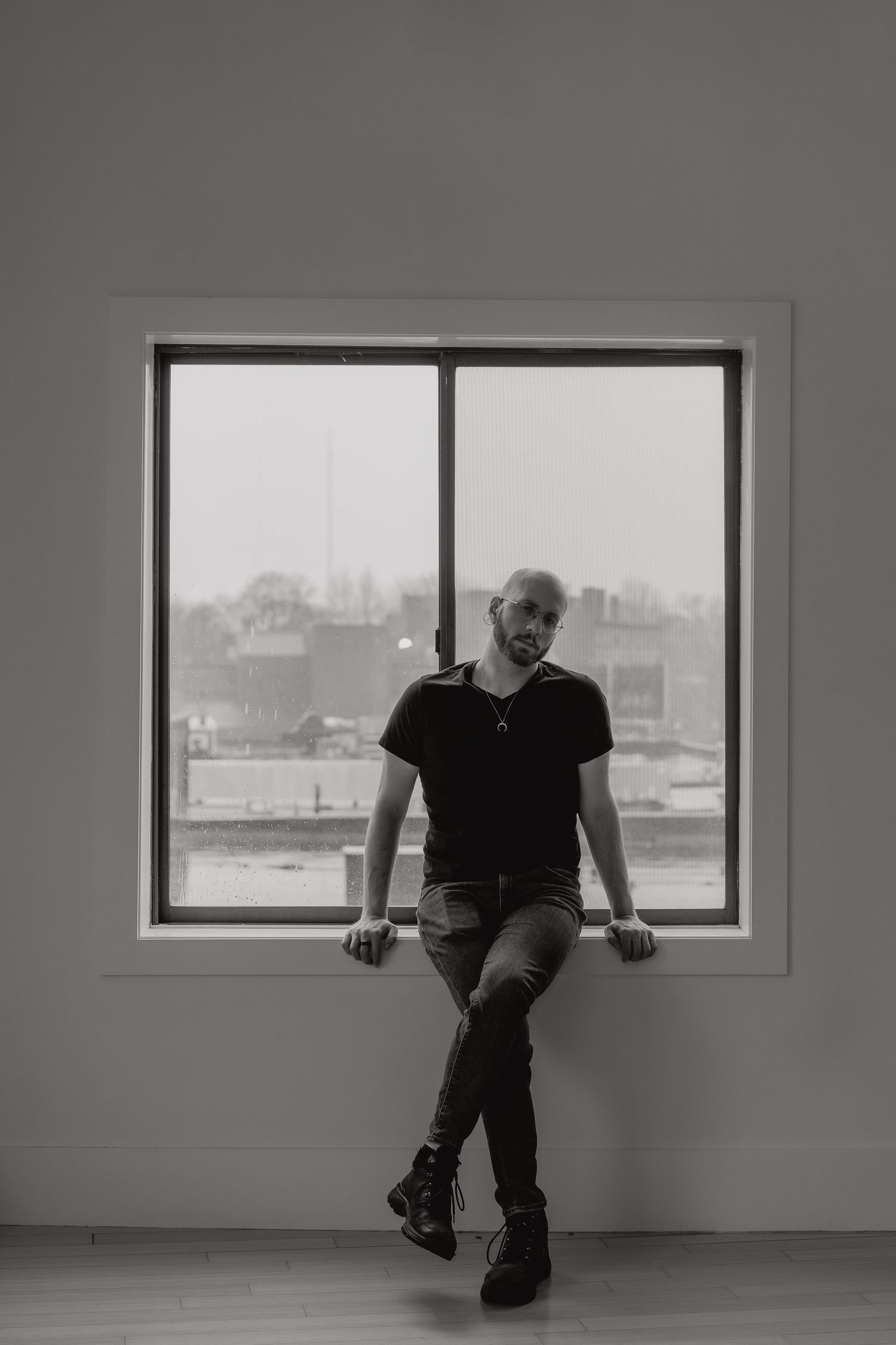 A front facing portrait of Michael in black and white leaning against the window sill