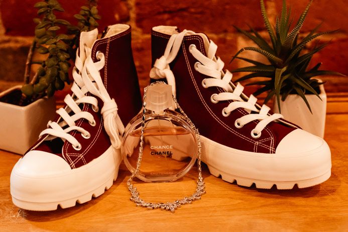 Burgundy platform sneakers arranged with a perfume bottle and chain on a wooden surface.