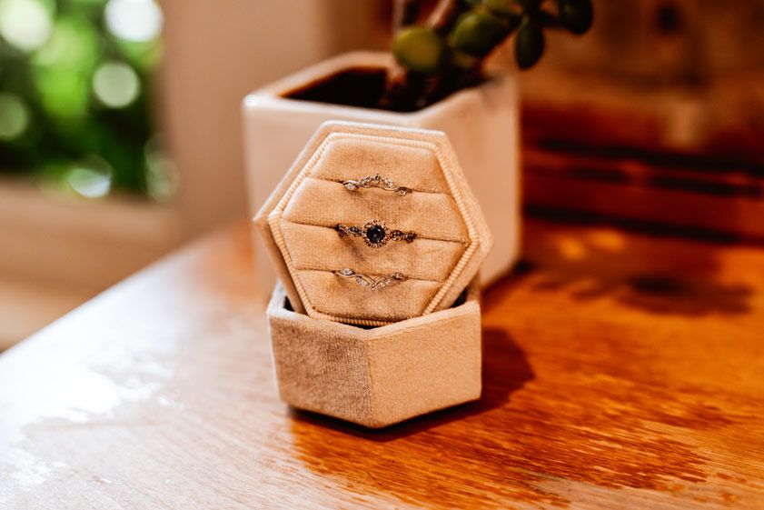 A hexagonal wooden ring box sits on a polished wooden surface in warm lighting.