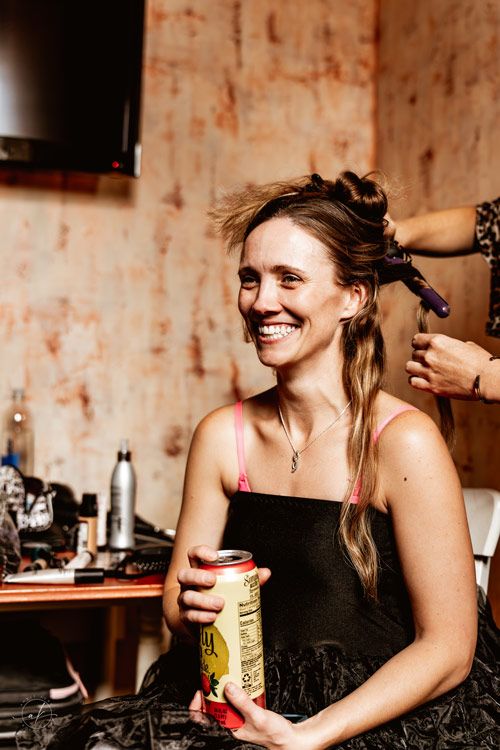 Candid moment of getting hair styled while holding a drink can during wedding preparations.