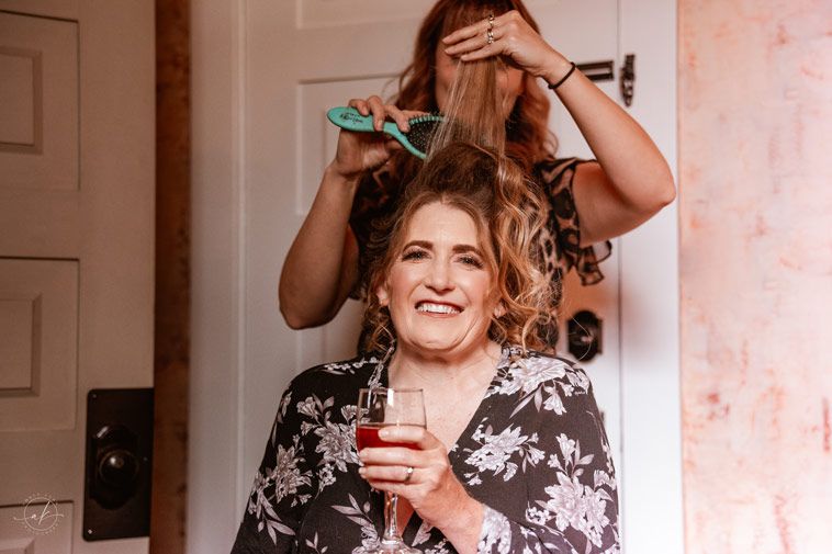 Getting hair styled while holding a glass during wedding preparations in a floral dress.