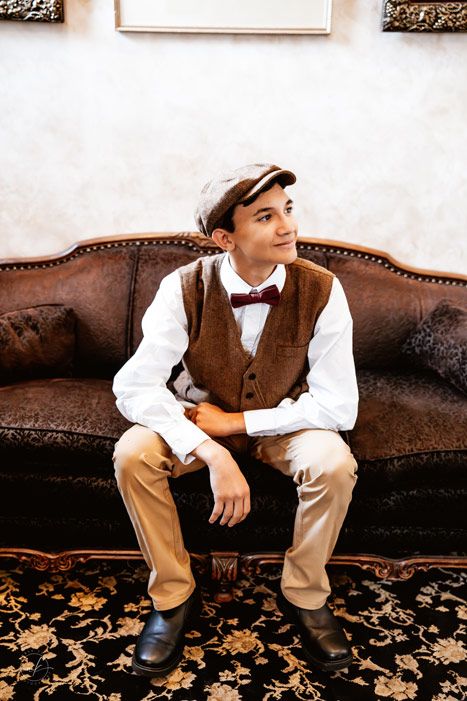 Vintage inspired formal portrait of someone in a brown vest and bowtie seated on an antique couch.