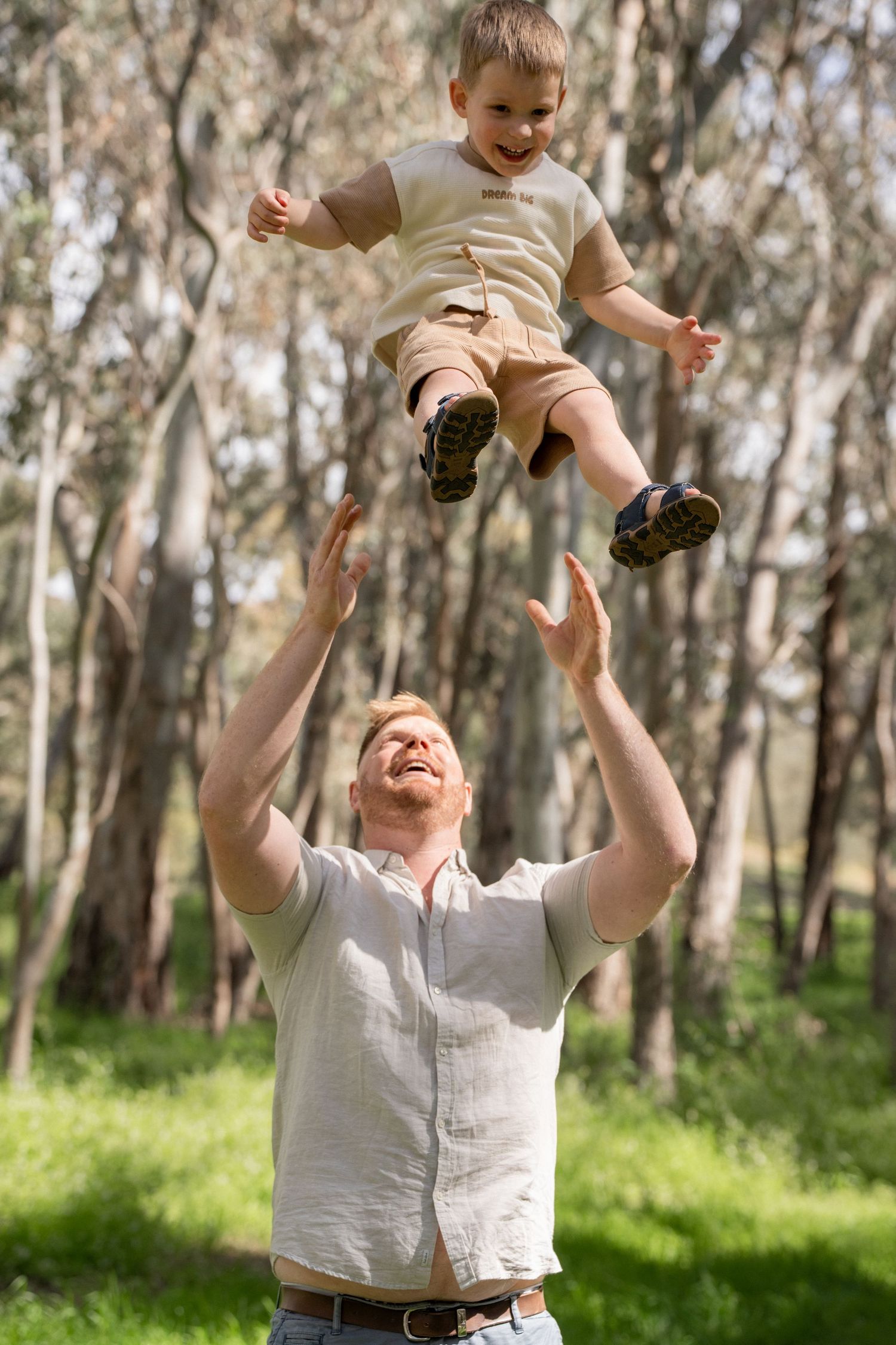 A tender beach moment as a parent lifts a small child in a white dress against a cloudy sky.