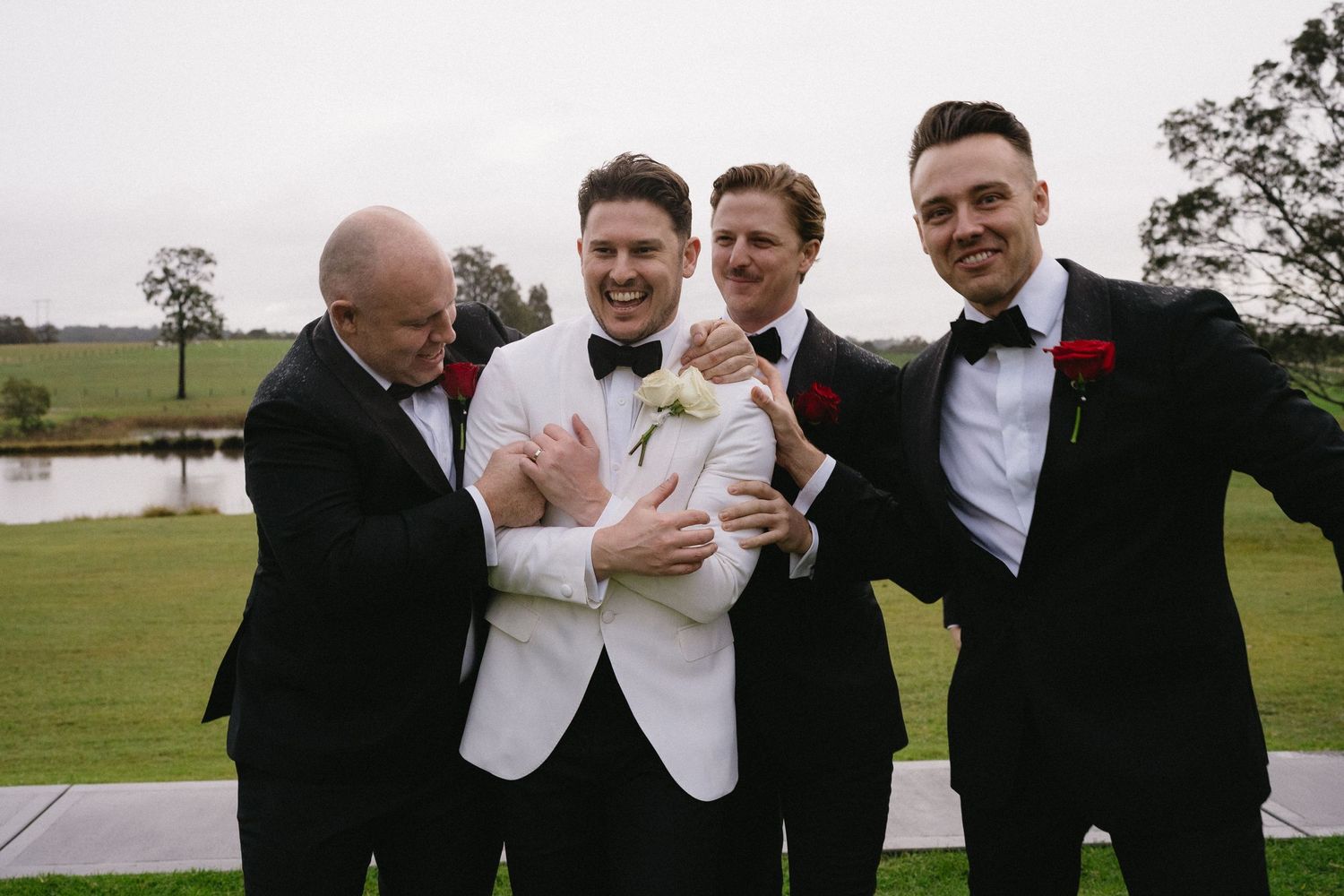 Groomsmen in formal attire share a candid moment on a golf course.