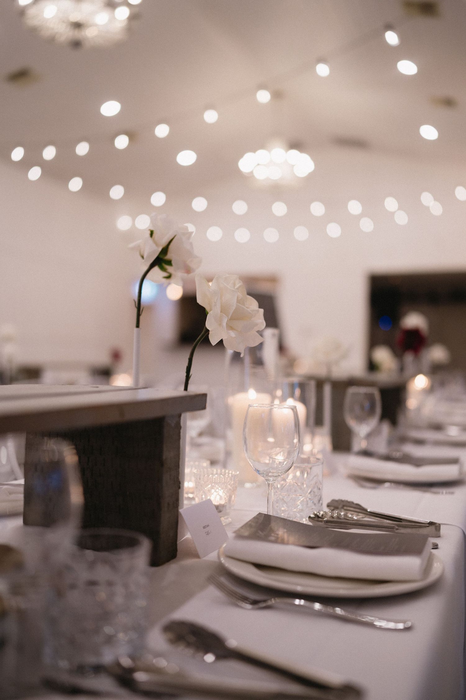 Wedding reception table with string lights overhead and elegant white place settings.