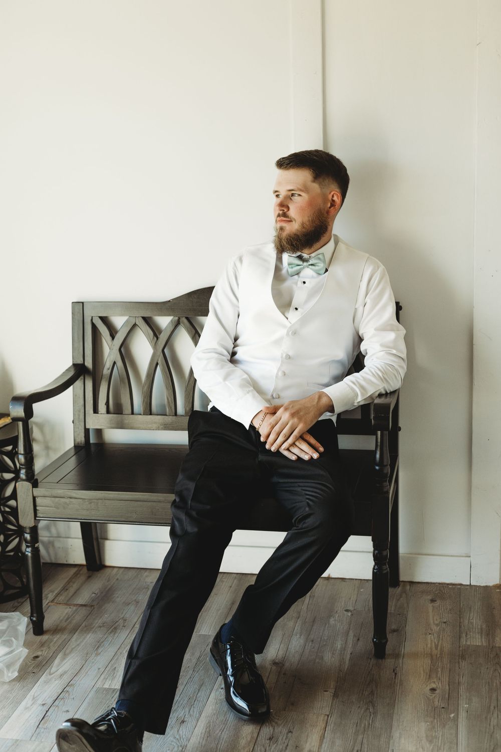 Person in white shirt and dark pants sitting on wooden bench against white wall.