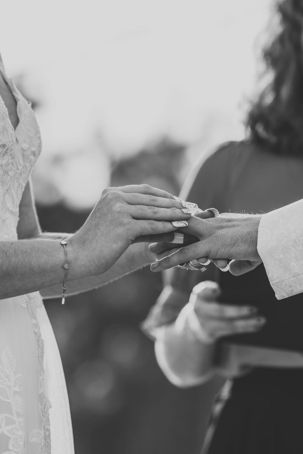 Close-up of hands exchanging wedding rings during ceremony in black and white.